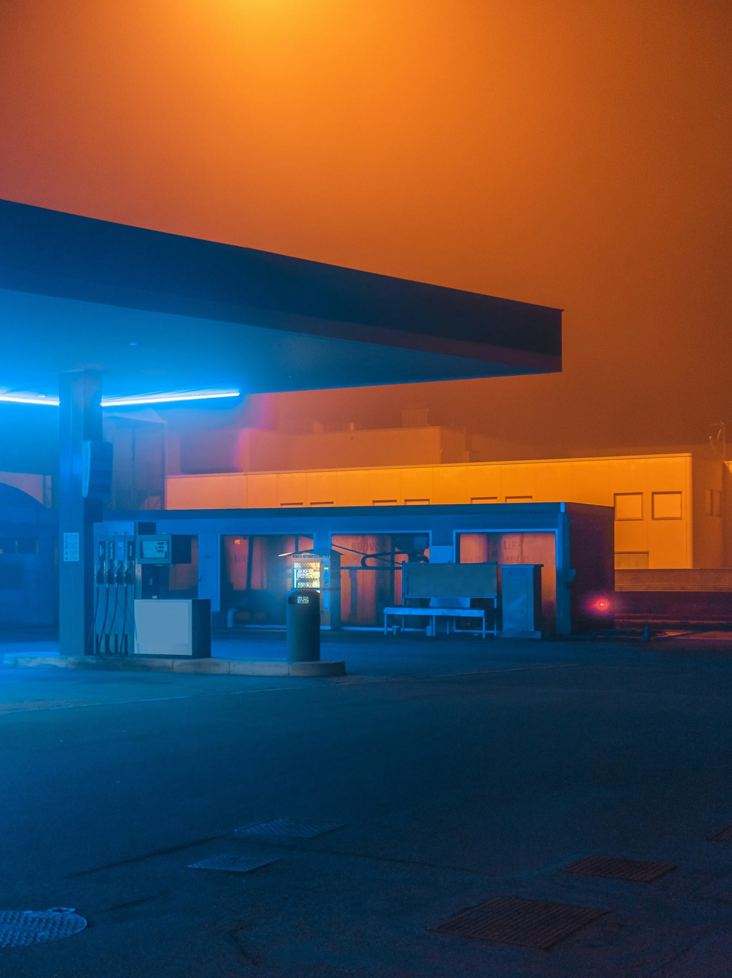 A gas station at night lit by blue neon in orange fog