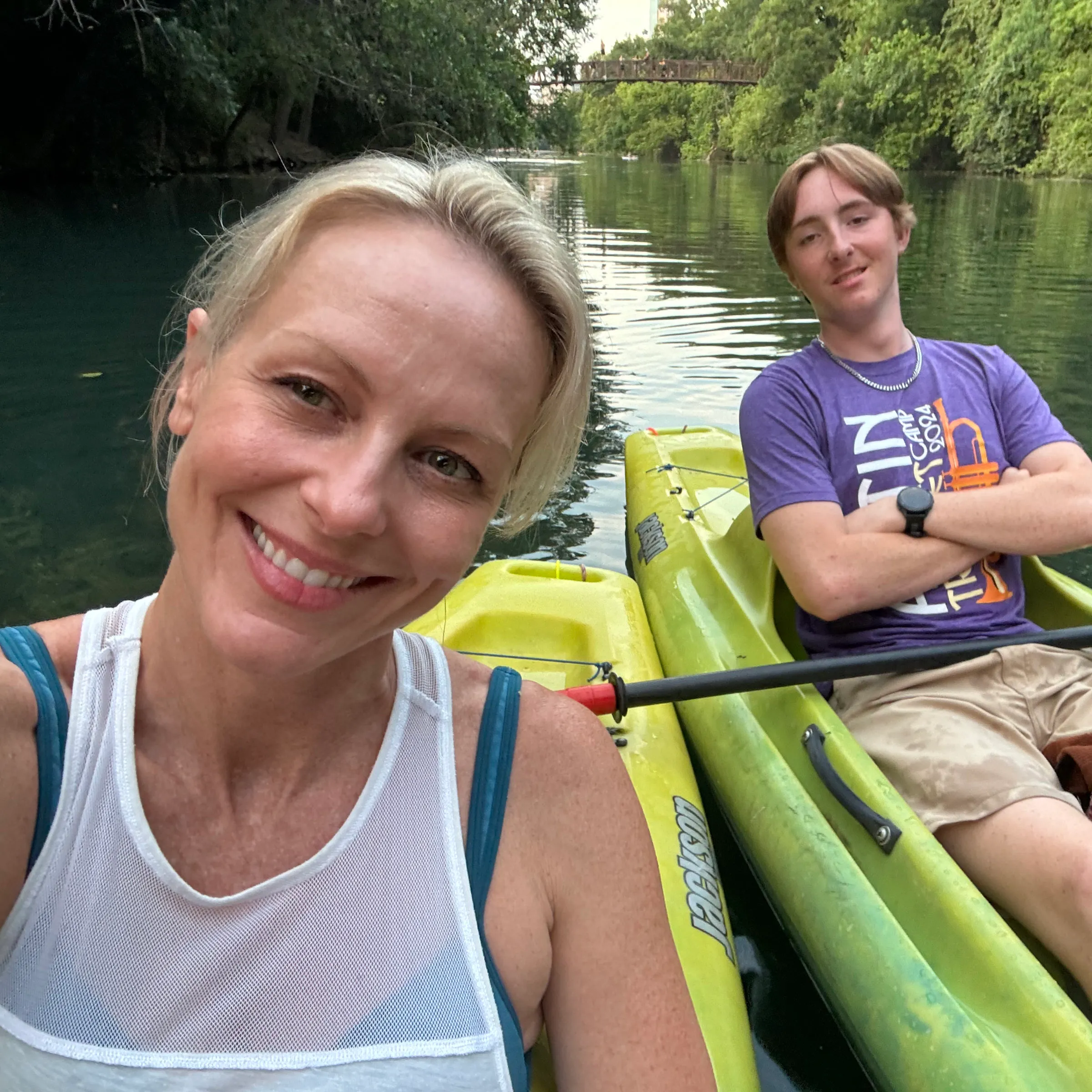 Rae and Jonas in green kayaks on a river, Rae smiling at the camera and Jonas with his arms crossed